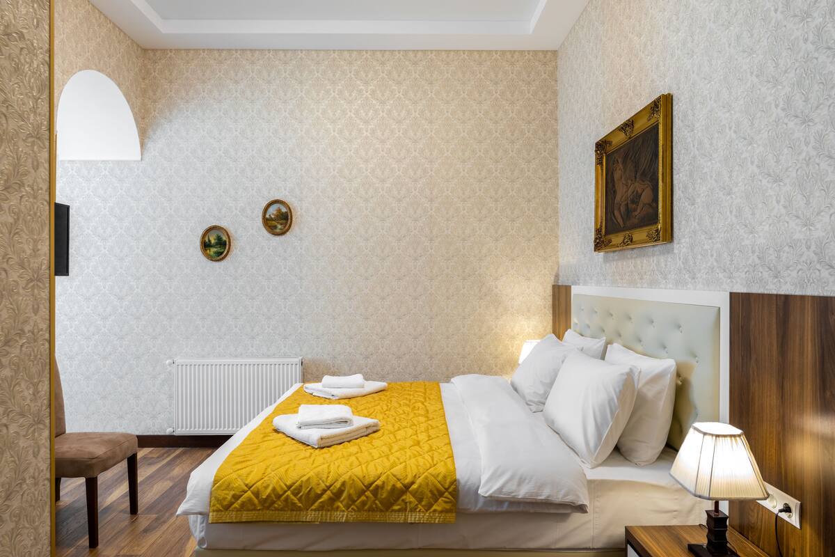 A hotel room with a bed, a chair, a bedside table with a lamp, and a wall with a framed picture.