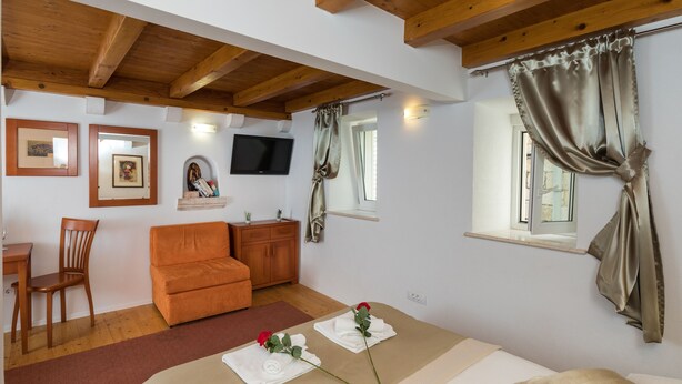 Quarto aconchegante com teto de madeira, um sofá, uma mesa pequena, uma televisão e uma janela com cortinas.