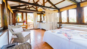 A room with a bed, wicker furniture, a small table, and a window with curtains. - Cubo's Mijas Finca Huerta Rica Bambu / shared pool / views (Mijas Pueblo)