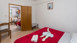 A hotel room with a bed, a chair, a table with a red tablecloth, and a small kitchenette in the background.