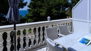 A balcony with a white railing, two wicker chairs, a table, and a covered umbrella.