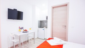Ein Hotelzimmer mit einem Bett, einem Schreibtisch mit Stühlen, einer kleinen Küchenzeile und einem an der Wand montierten Fernseher.