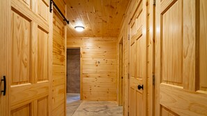 Un couloir en bois avec un plancher en béton, des portes en bois et un luminaire au plafond.