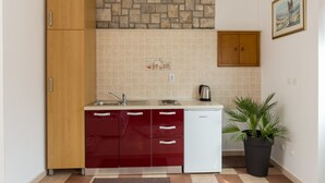 A compact kitchen with a stone backsplash, wooden cabinets, a white dishwasher, and a potted plant. - Apartments Dia - Studio Apartment with Terrace (Dubrovnik)