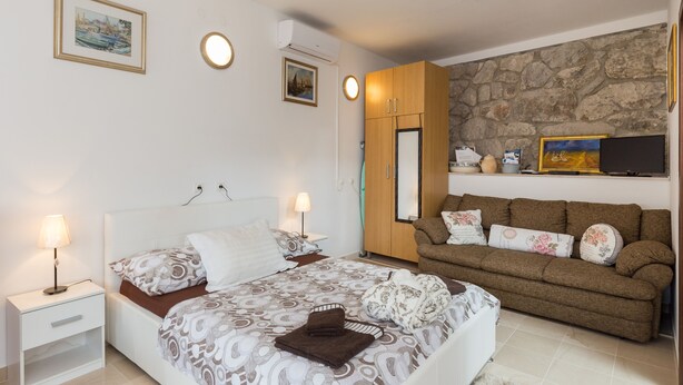 A bedroom with a bed, bedside tables, a sofa, a TV, and a stone wall. - Apartments Dia - Studio Apartment with Terrace (Dubrovnik)