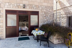 A stone building with a wooden door and windows, a table with a floral tablecloth, and a chair outside. - Apartments Dia - Studio Apartment with Terrace (Dubrovnik)