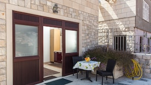 A patio area with a table and chairs, a door leading inside, and a stone wall with a hose. - Apartments Dia - Studio Apartment with Terrace (Dubrovnik)