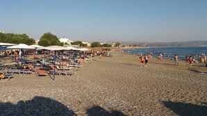 A beach with sun loungers and umbrellas, a rocky shoreline, and a clear sky. - Studio with sea view (Kokkinos Pirgos)
