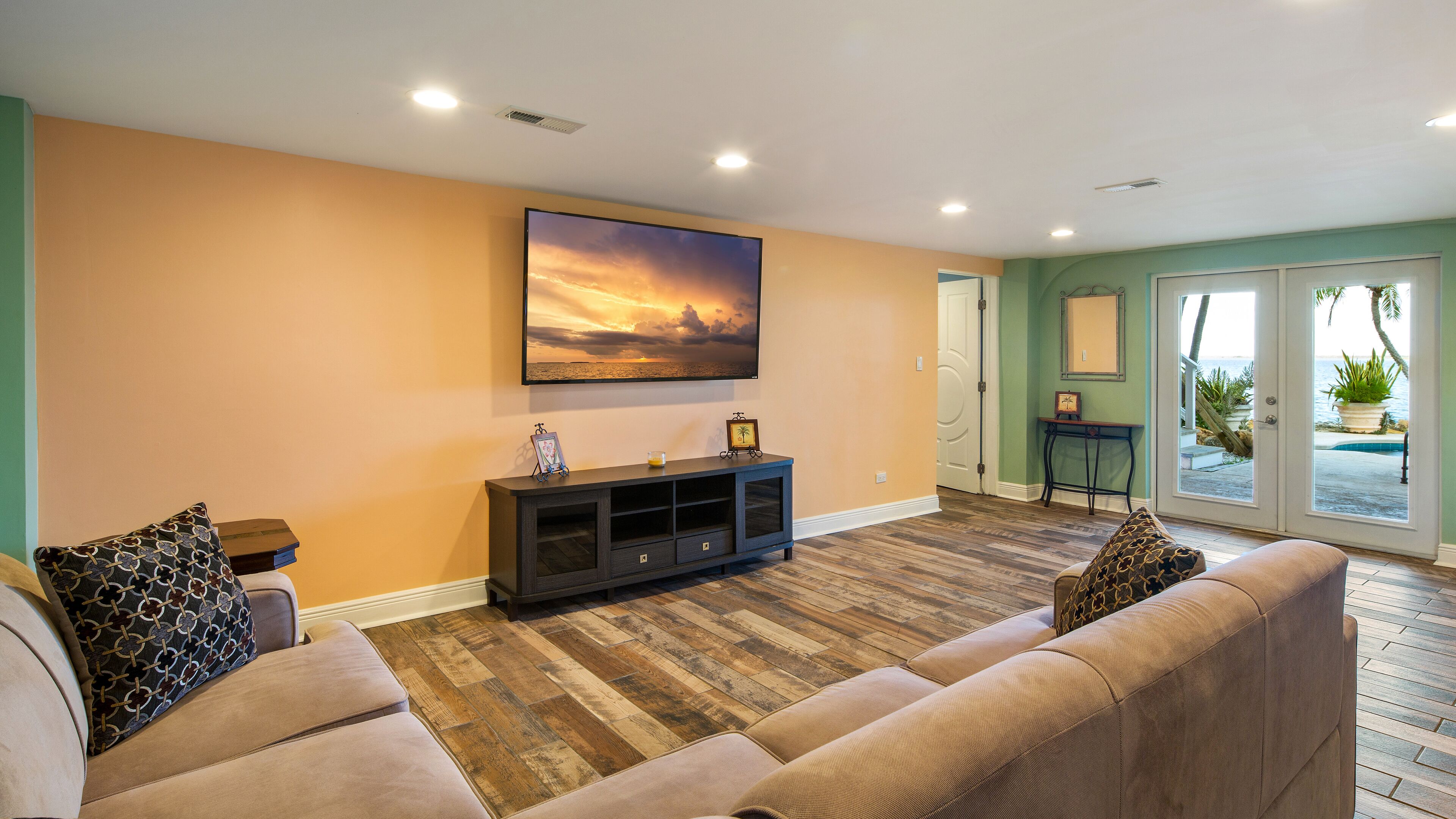 A living room with a large sofa, a dark console table, and a painting of a sunset.