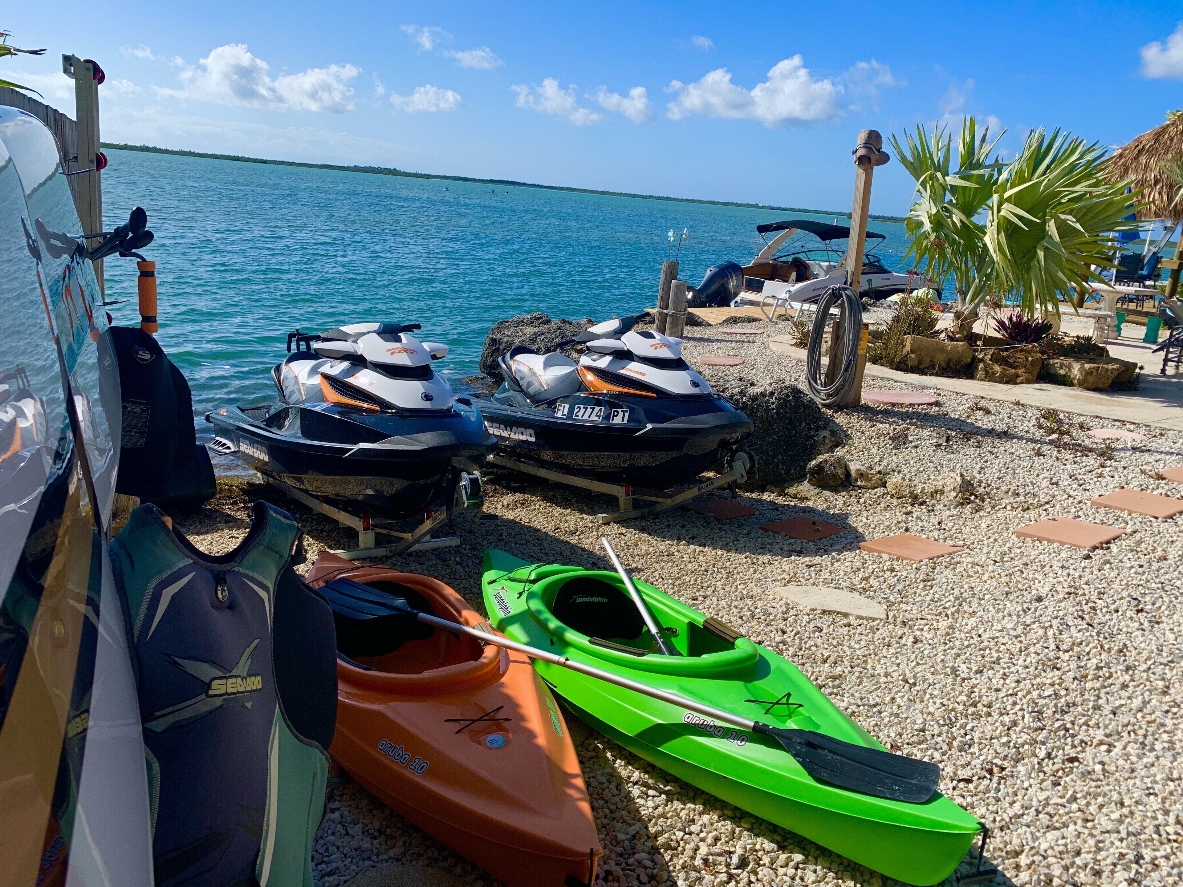 Un moll de vaixells amb dues motos aquàtiques i un kayak verd a la riba de pedres.