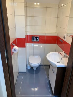 A small bathroom with a toilet, sink, and a red accent wall. - Domki Magnolia (Kolobrzeg)