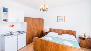 Une chambre avec un lit en bois, un petit coin cuisine, une armoire en bois et un lustre.