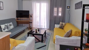 A living room with a grey sofa, a yellow sofa, a coffee table, a TV on a wooden stand, and a bookshelf. - Marie-Claire's Home , Sykies Thessaloniki (Sikies)