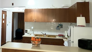 A kitchen with wooden cabinets, a white countertop, a bowl of oranges, a coffee maker, and a microwave. - Marie-Claire's Home , Sykies Thessaloniki (Sikies)