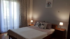 A neatly made bed with a white bedspread and pillows, two bedside lamps, a framed artwork on the wall, and a window with sheer curtains. - Marie-Claire's Home , Sykies Thessaloniki (Sikies)