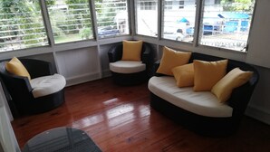 A room with a wooden floor, a black and white sofa, a black chair, and a glass table. - Casa en Gamboa al lado Canal de Panama (Colon)