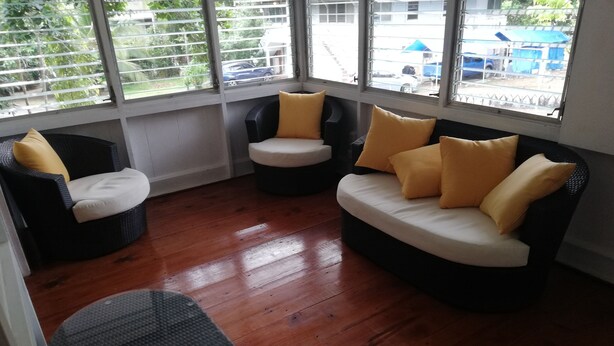 Una habitación con piso de madera, un sofá blanco y negro, una silla negra y una mesa de vidrio.