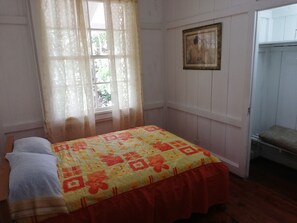 A room with a bed, a window with sheer curtains, a painting on the wall, and a wardrobe.