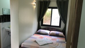 Ein Schlafzimmer mit Bett, einem Fenster mit Vorhängen, einer Nachttischlampe und einem Badezimmer mit Waschbecken und Spiegel.