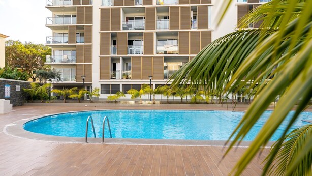 Un hotel moderno con piscina, terraza de madera y balcones con barandillas.