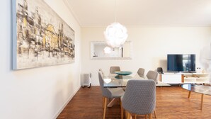 Una sala de estar moderna con comedor, un cuadro abstracto grande, un televisor y una lámpara de araña original.