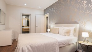 Un dormitorio con una cama grande, mesitas de noche, un espejo y un baño visible a través de una puerta abierta.