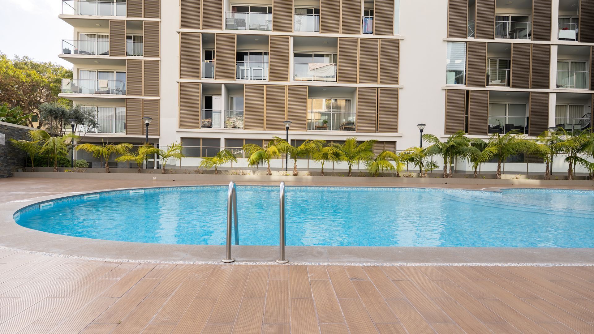 Um hotel moderno com piscina, várias varandas e palmeiras.