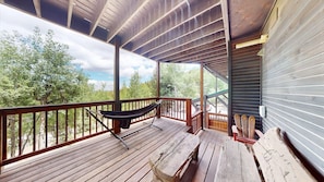 A wooden deck with a hammock, benches, and a view of trees.
