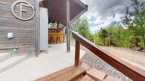 A wooden building with a covered outdoor area, a bar, and a gravel path leading to a forest. - Views | WiFi | Fireplace | Elk Ridge Lodge (Angel Fire)