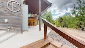 Un bâtiment en bois doté d’un espace extérieur couvert, d’un bar et d’un chemin de gravier menant à une forêt.
