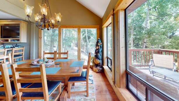 A wooden interior with a dining area, large windows, and a view of trees. - Views | WiFi | Fireplace | Elk Ridge Lodge (Angel Fire)