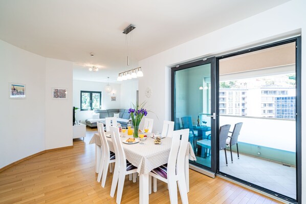 Comedor con una mesa dispuesta para cuatro, vista al balcón y una cocina moderna al fondo.