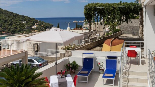 A balcony with lounge chairs, a table, and a view of the sea. - Stuck in the Moment Apartment - One Bedroom Apartment with Terrace and Sea View (Dubrovnik)