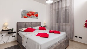 A modern bedroom with a large bed, two bedside tables with lamps, a decorative wall piece, and sheer curtains. - Stuck in the Moment Apartment - One Bedroom Apartment with Terrace and Sea View (Dubrovnik)