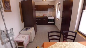 A compact kitchen with dark cabinets, a small dining table with chairs, and a refrigerator. - Apartment in Premantura with Garage near Kamenjak (Medulin)