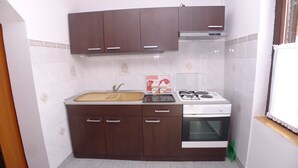 A compact kitchen with dark brown cabinets, a stainless steel sink, and a white stove. - Apartment in Premantura with Garage near Kamenjak (Medulin)