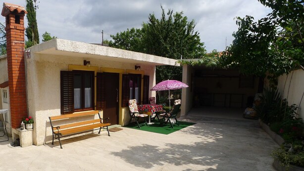 A small building with a bench and a table with chairs under a purple umbrella. - Apartment in Premantura with Garage near Kamenjak (Medulin)
