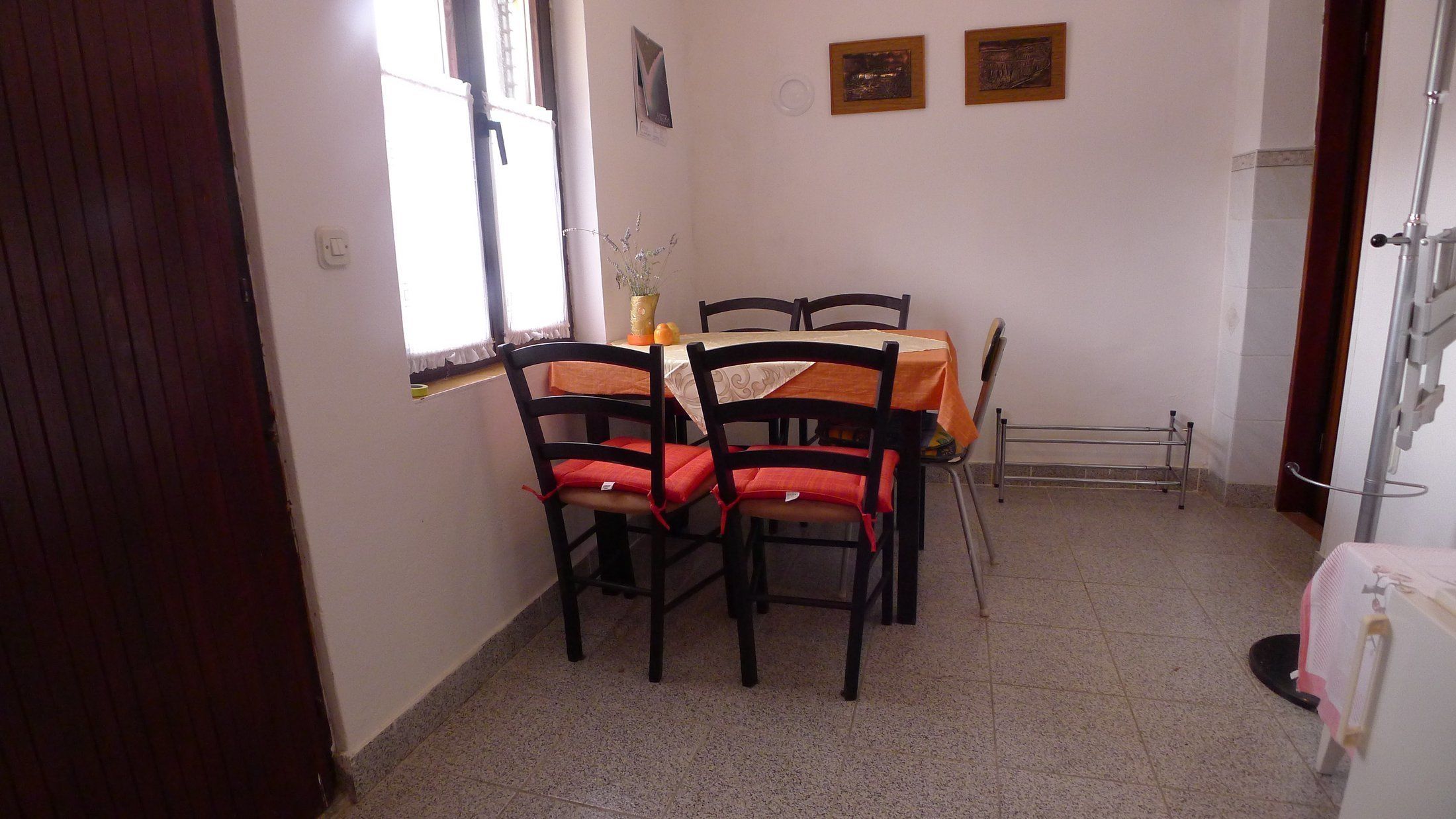A dining area with a round table, four chairs with red cushions, a vase with flowers, and two framed pictures on the wall.