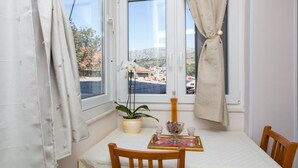 Een kamer met een gedekte tafel voor twee personen, een potplant en uitzicht op een stad door een raam.