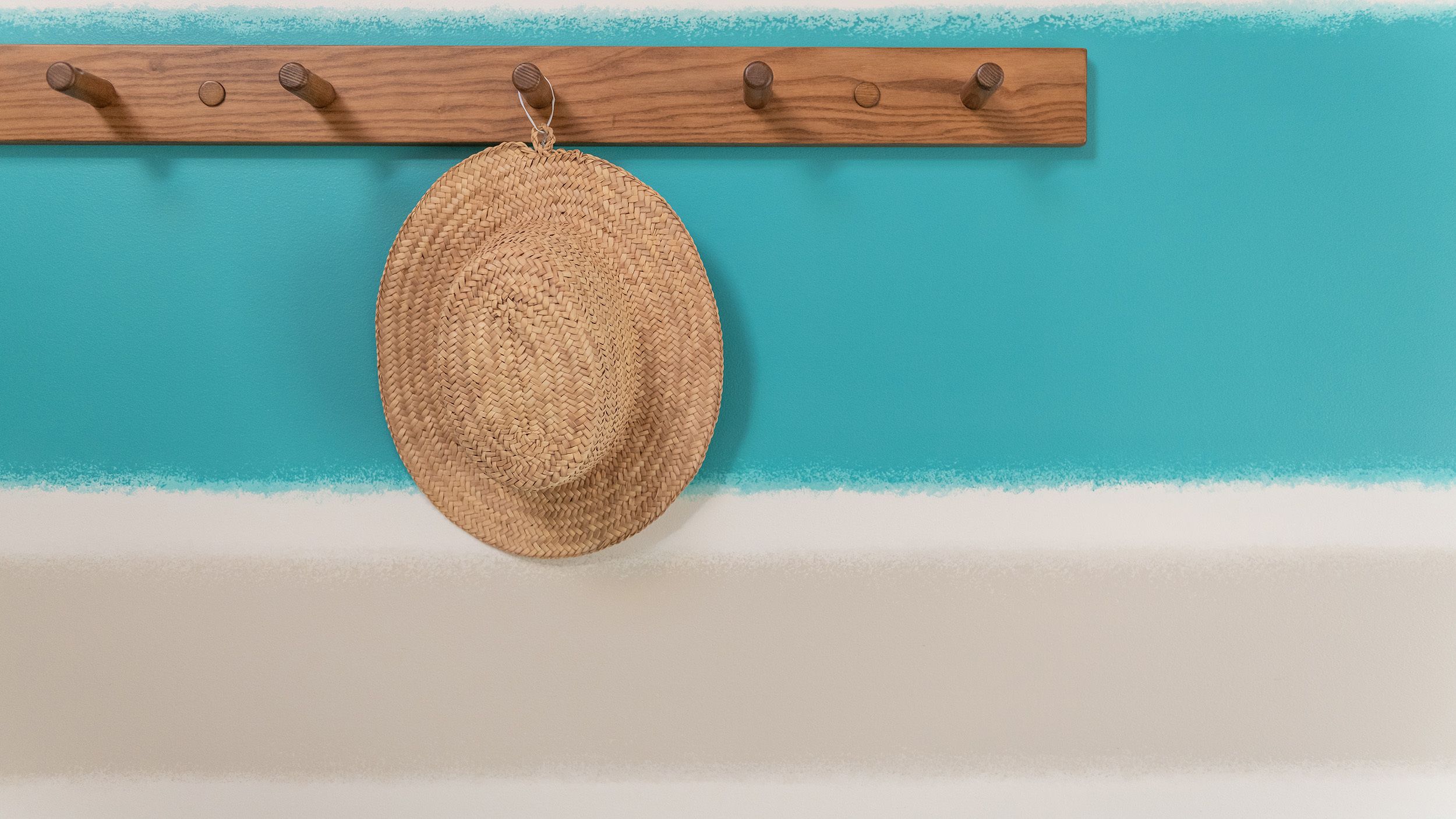 A straw hat hanging on a wooden rack against a wall with a blue and white color scheme.