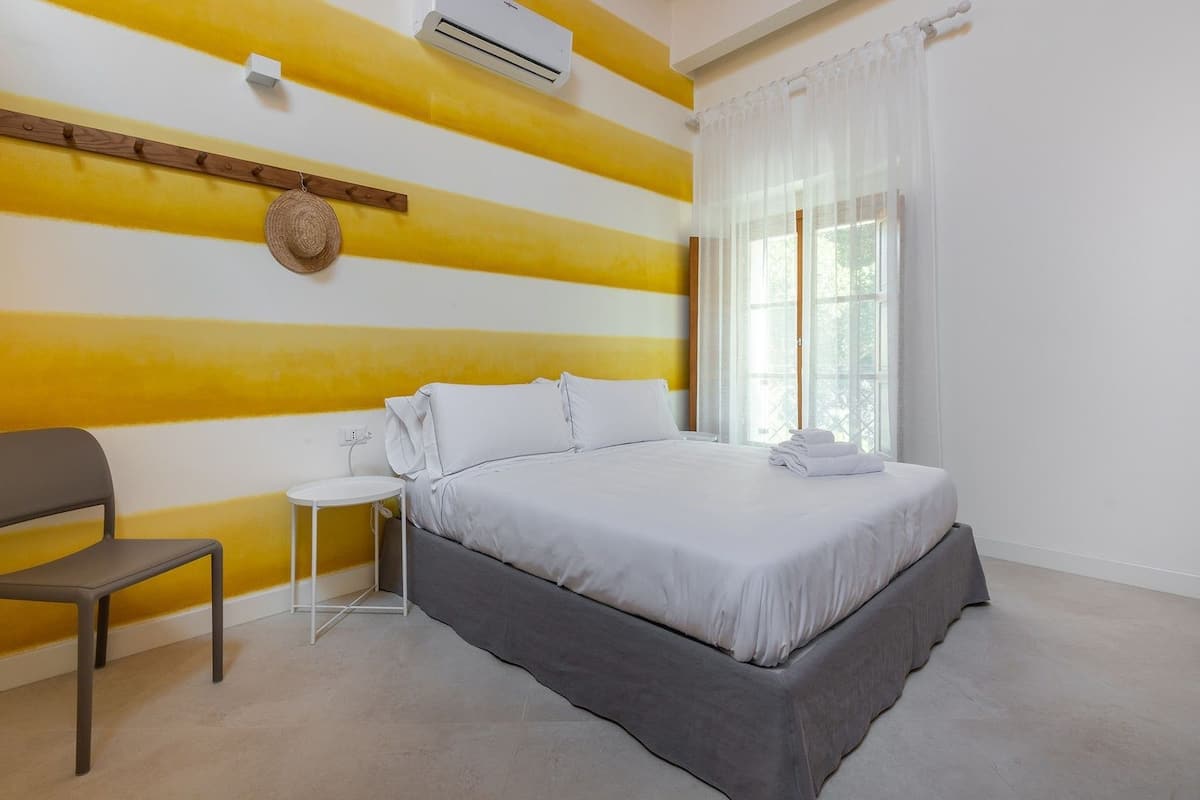 A bedroom with a bed, a chair, a small table, and a window with curtains.