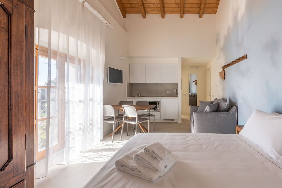 A modern hotel room with a large bed, a desk, and a kitchenette.