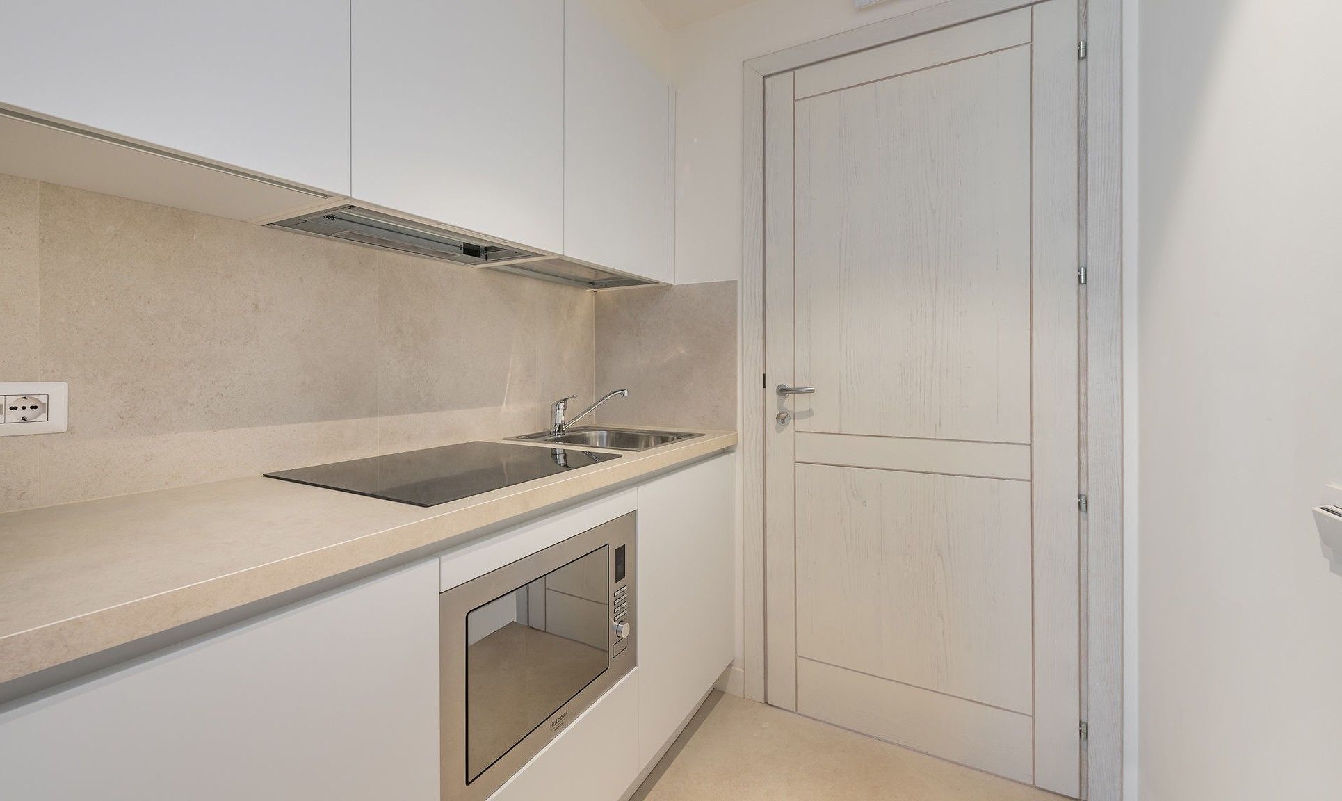 Una cocina compacta con microondas integrado, un lavamanos y una campana extractora.