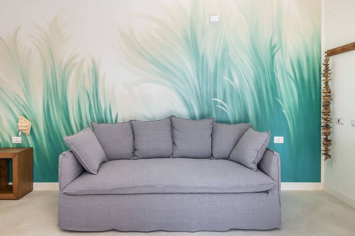 A grey sofa in a room with a wall mural of green foliage.