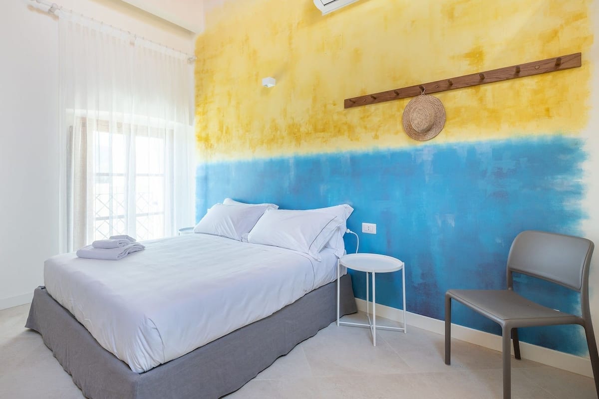 A bedroom with a bed, a chair, and a wall with a wooden shelf.