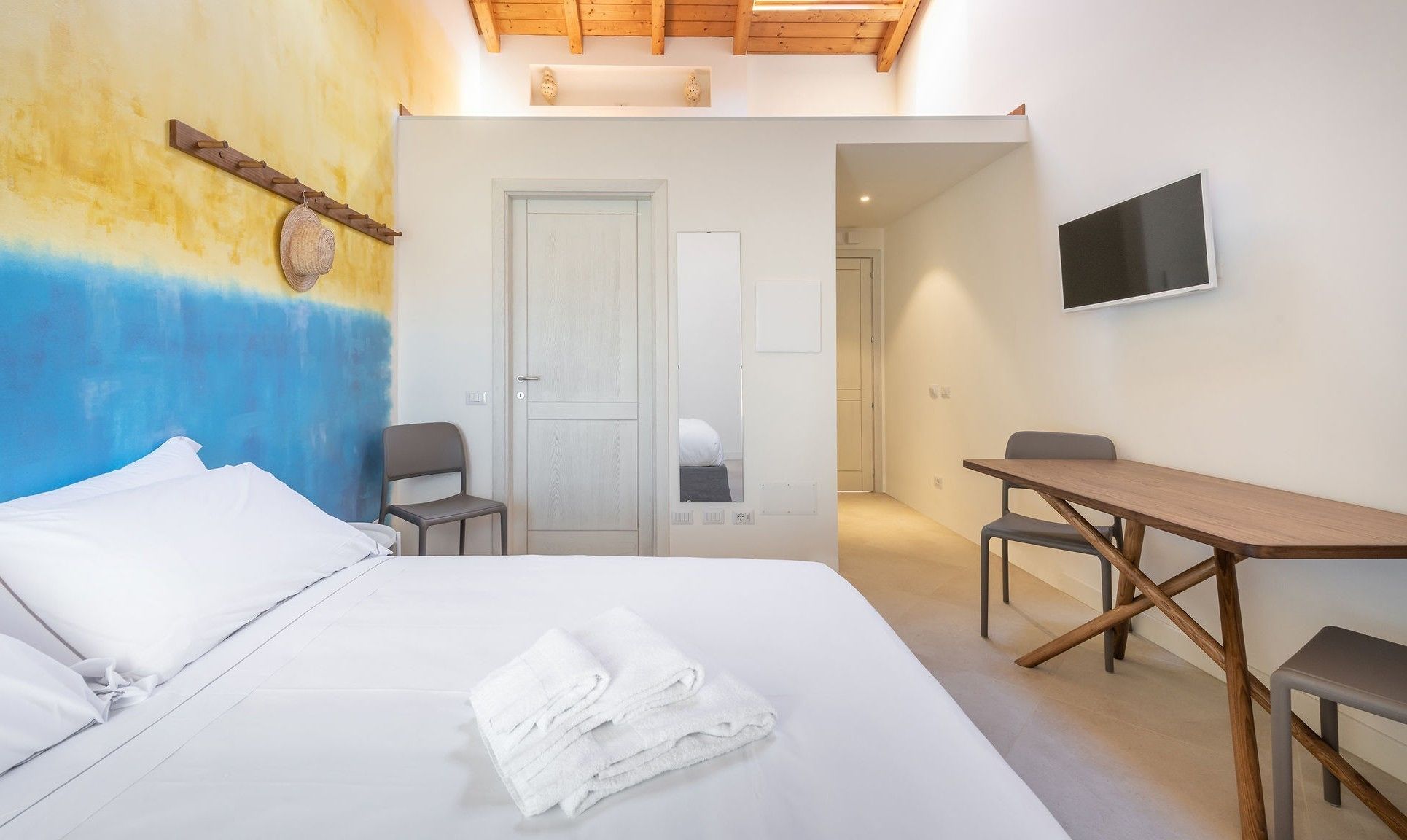 A bedroom with a bed, a desk, and a chair. There is a TV mounted on the wall.