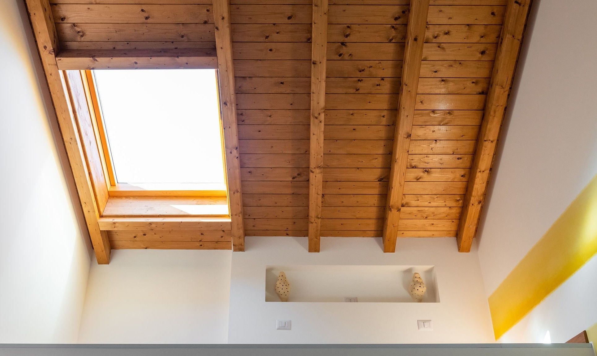 Een kamer met een schuin houten plafond, dakraam en een witte muur met twee kleine nisjes.
