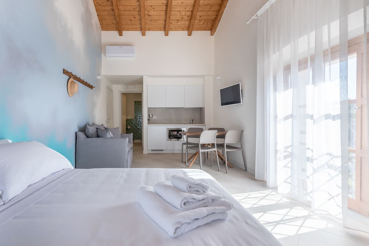 A bedroom with a bed, a desk, and a kitchenette.