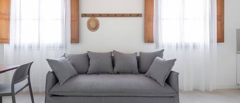 Una sala de estar moderna con un sofá gris, un perchero de madera y un tapiz tejido en la pared.