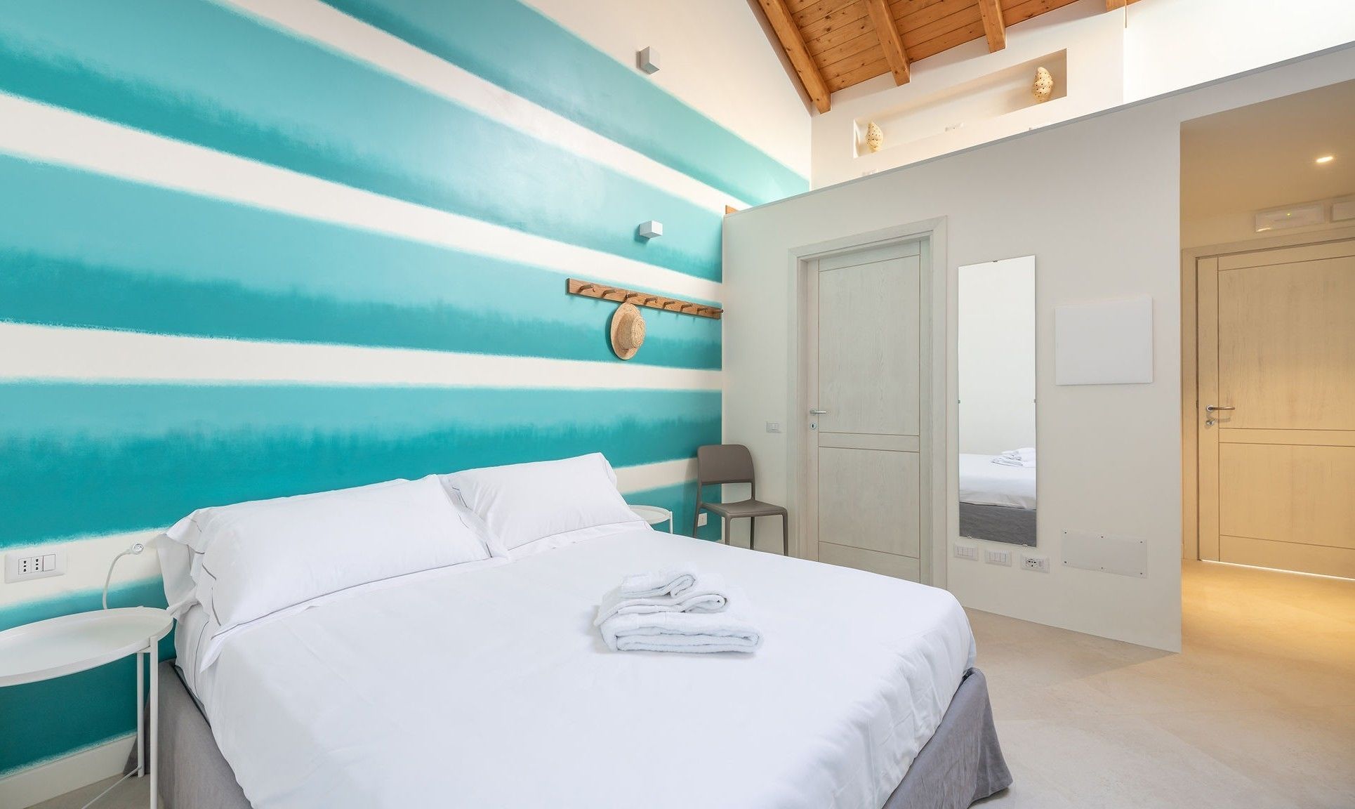 A bedroom with a bed, a chair, a wall-mounted hat, and a door leading to another room.